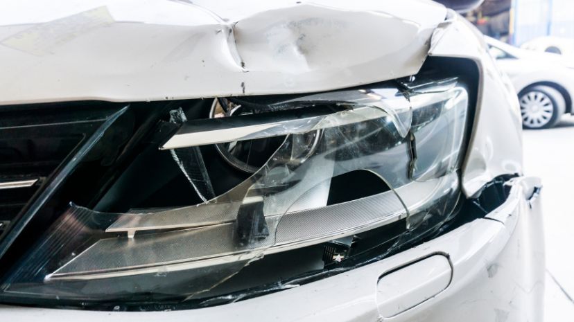 Przednia część białego samochodu uszkodzona w wyniku stłuczki ze zbitym reflektorem