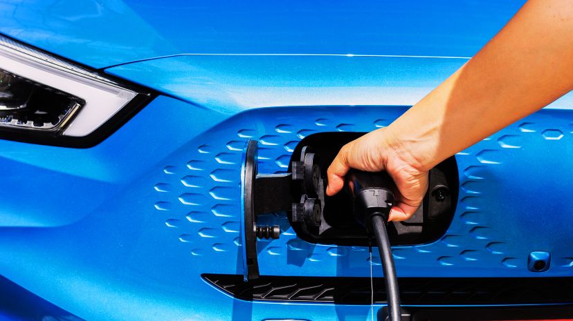 Zbliżenie na rękę podłączającą kabel ładowania do niebieskiego samochodu elektrycznego.