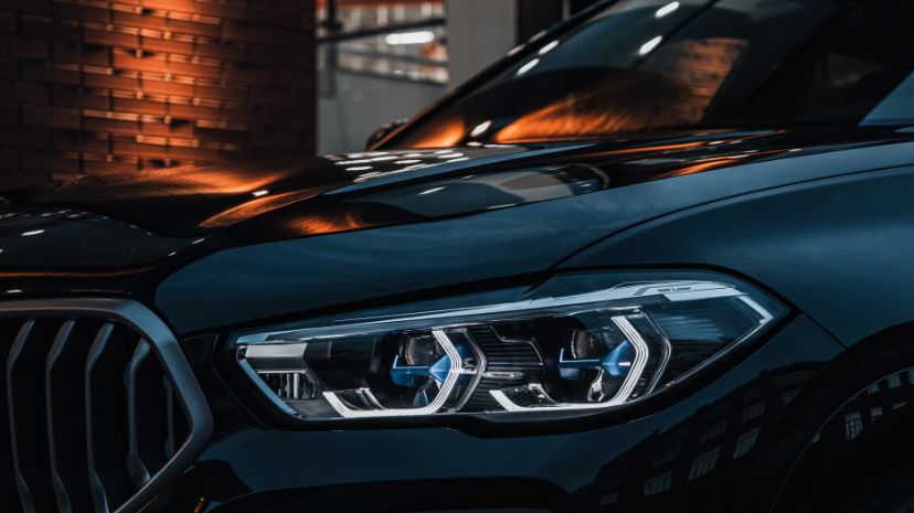 Zbliżenie na reflektor nowoczesnego samochodu z eleganckim, dynamicznym designem marki BMW, z refleksami świetlnymi na karoserii