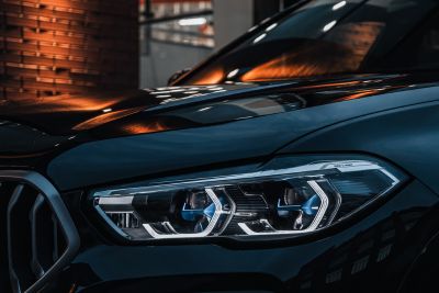 Zbliżenie na reflektor nowoczesnego samochodu z eleganckim, dynamicznym designem marki BMW, z refleksami świetlnymi na karoserii