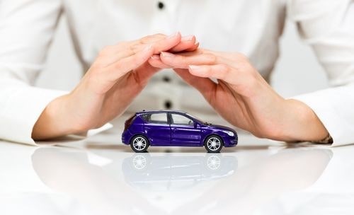 Dłonie kobiety w białej koszuli osłaniające fioletowy samochód zabawkę