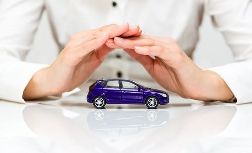 Ubezpieczenie GAP na FmLeasing.pl Dłonie kobiety w białej koszuli osłaniające fioletowy samochód zabawkę