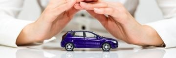 Dłonie chroniące zabawkowy fioletowy samochód osobowy