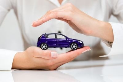 Kobiece dłonie chroniące zabawkowy samochód osobowy symbolizujące ochronę ubezpieczenia GAP
