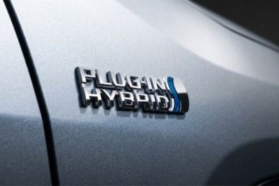 Zbliżenie na chromowany emblemat „Plug-in Hybrid” na karoserii samochodu w kolorze srebrny metalik z błękitnym połyskiem