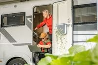 Para przy kamperze – kobieta w drzwiach, mężczyzna siedzi ze sprzętem elektronicznym na kolanach, planując podróż lub sprawdzając informacje.