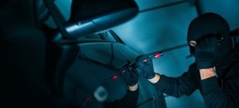 Zamaskowany mężczyzna w ciemnym garażu próbujący włamać się do samochodu