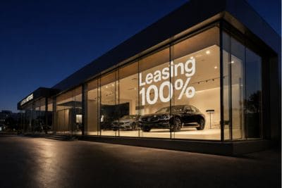 Nowoczesny salon samochodowy o zmierzchu z napisem „Leasing 100%” na przeszklonej fasadzie
