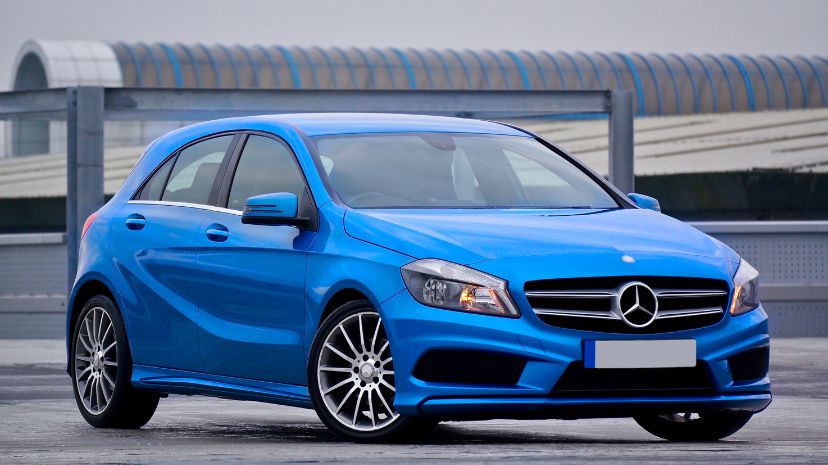 Niebieski samochód Mercedes-Benz klasy A zaparkowany na tle nowoczesnej architektury, widoczny z przodu i z boku.