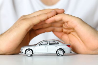 Dłonie ułożone w ochronnym geście nad miniaturowym modelem samochodu, symbolizujące bezpieczeństwo i ochronę pojazdu, nawiązujące do ubezpieczenia GAP.