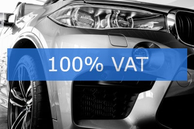 Samochód osobowy z nałożonym napisem '100% VAT' na niebieskim tle
