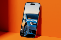 Smartfon na pomarańczowym tle, na którego ekranie widoczny jest jasny nowoczesny samochód