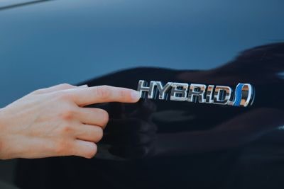 Emblemat „Hybrid” na nadwoziu samochodu, wskazywany palcem – symbol hybryd plug-in (PHEV).