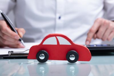 Czerwony samochód zabawka stojący na biurku przed ubranym w białą koszulę mężczyzną robiącym obliczenia na kalkulatorze