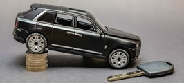 Model luksusowego SUV-a balansujący na stosie monet, symbolizujący utratę wartości samochodów, obok kluczyka samochodowego