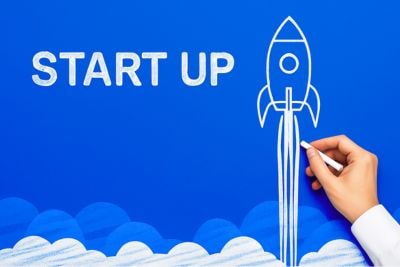 Start-up – ręka rysuje kredą startującą rakietę na niebieskim tle, symbol szybkiego startu firmy i leasingu na rozpoczęcie działalności.