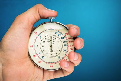 Ręka trzymająca stoper na niebieskim tle, symbolizujący czas i szybkość działania